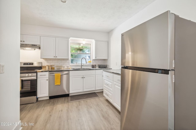 kitchen with appliances with stainless steel finishes, extractor fan, sink, light hardwood / wood-style floors, and white cabinetry