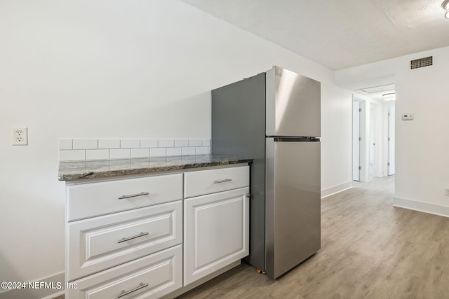 kitchen featuring white cabinets, stainless steel fridge, light hardwood / wood-style floors, and dark stone counters