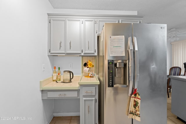 kitchen with a textured ceiling, light tile patterned flooring, and stainless steel refrigerator with ice dispenser