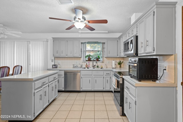 kitchen with decorative backsplash, appliances with stainless steel finishes, a textured ceiling, sink, and light tile patterned flooring