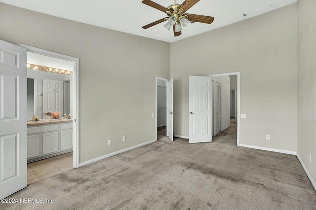 unfurnished bedroom featuring a spacious closet, light colored carpet, ensuite bath, and ceiling fan