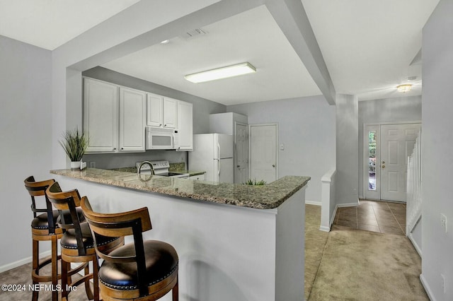 kitchen featuring kitchen peninsula, light stone countertops, white cabinets, and white appliances