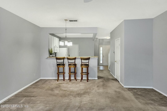 kitchen with pendant lighting, white appliances, carpet floors, a kitchen bar, and kitchen peninsula