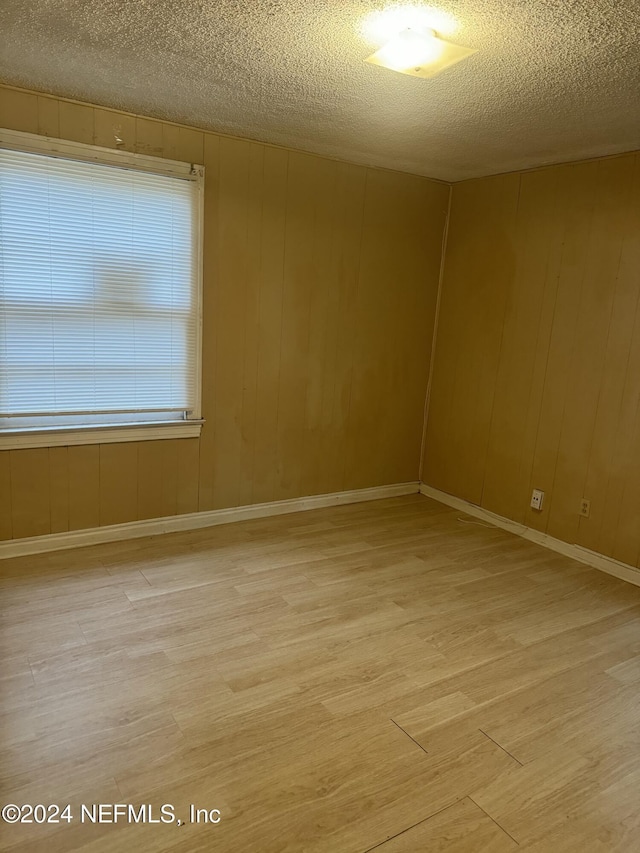 empty room featuring wood walls, wood-type flooring, and a textured ceiling