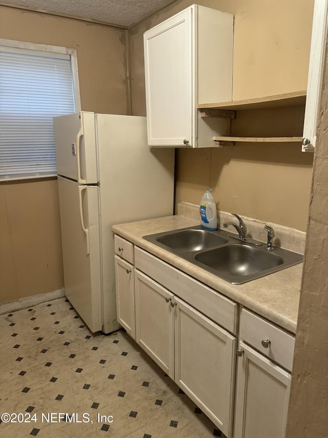 kitchen featuring white cabinets, white fridge, sink, and a textured ceiling