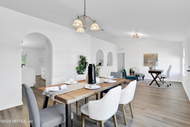 dining area with hardwood / wood-style flooring, lofted ceiling, and a notable chandelier