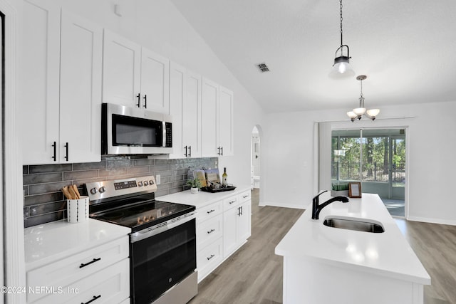 kitchen featuring stainless steel appliances, sink, decorative light fixtures, lofted ceiling, and an island with sink