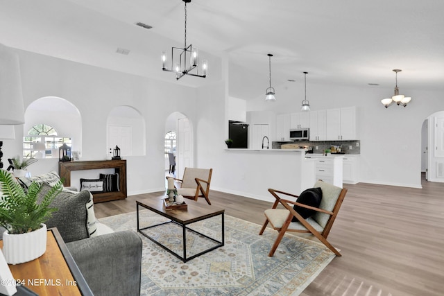 living room featuring light hardwood / wood-style floors, sink, high vaulted ceiling, and an inviting chandelier