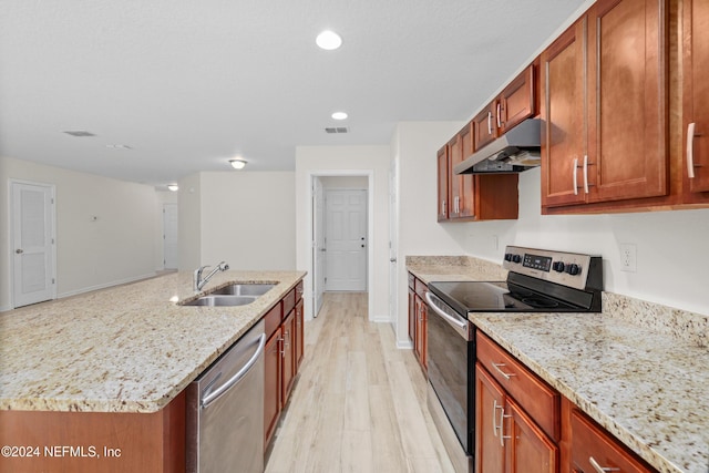 kitchen with appliances with stainless steel finishes, light stone counters, sink, a center island with sink, and light hardwood / wood-style flooring