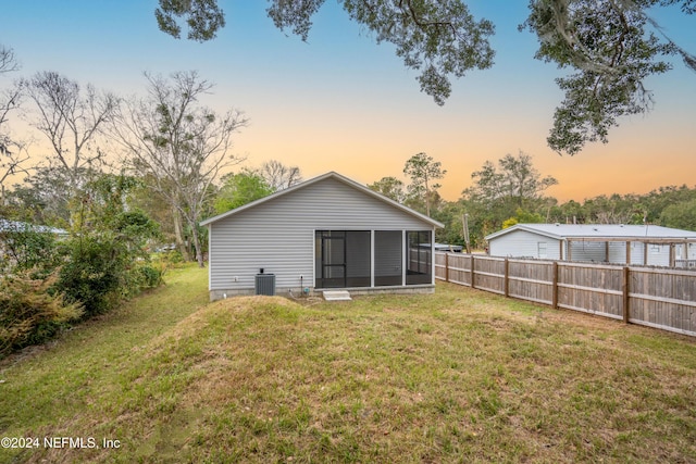 back house at dusk with a sunroom, a yard, and central AC