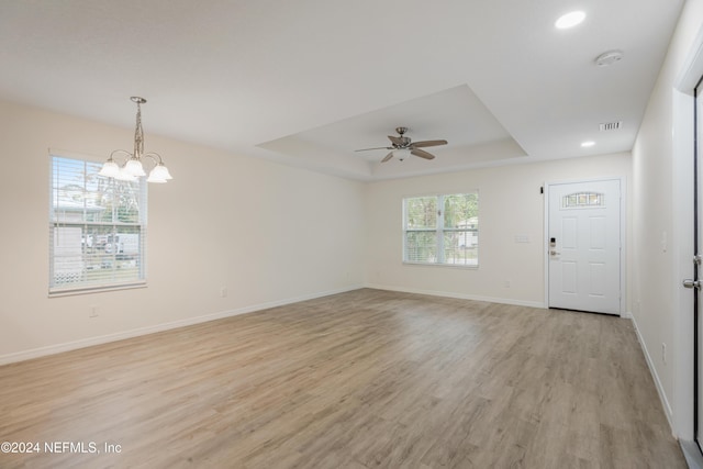 interior space featuring a raised ceiling, light hardwood / wood-style flooring, and ceiling fan with notable chandelier