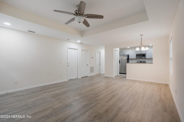 unfurnished living room featuring ceiling fan with notable chandelier and light hardwood / wood-style floors