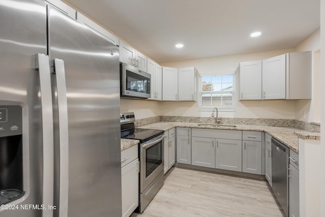 kitchen with white cabinets, sink, light stone countertops, appliances with stainless steel finishes, and light hardwood / wood-style floors