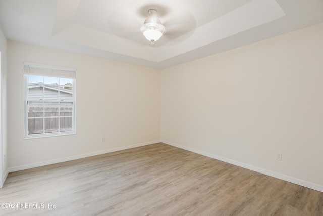 spare room featuring a tray ceiling, ceiling fan, and light wood-type flooring