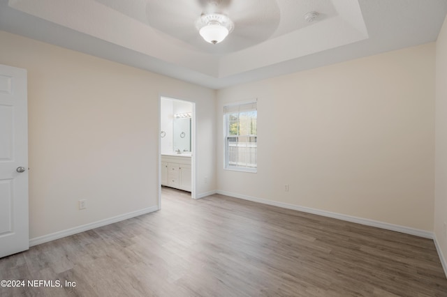 unfurnished bedroom with ensuite bath, a tray ceiling, ceiling fan, sink, and hardwood / wood-style flooring