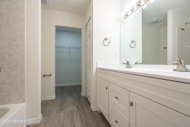 bathroom with hardwood / wood-style floors, vanity, a textured ceiling, and tiled shower / bath