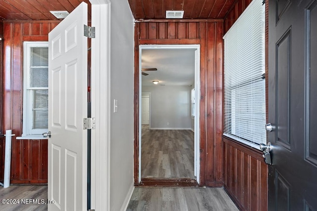 hallway featuring light wood-type flooring, wooden walls, and wood ceiling