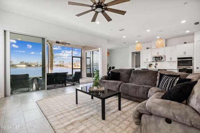 tiled living room with ceiling fan and a water view