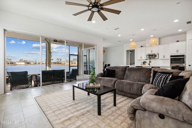 living room featuring light tile patterned floors, a water view, and ceiling fan