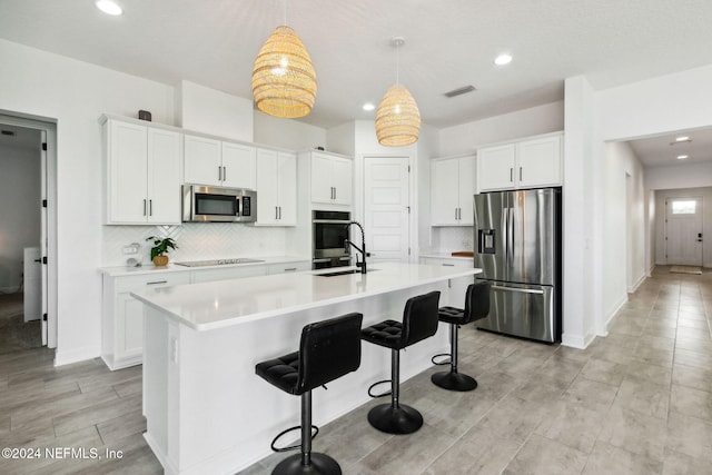 kitchen featuring white cabinets, appliances with stainless steel finishes, a center island with sink, and decorative light fixtures