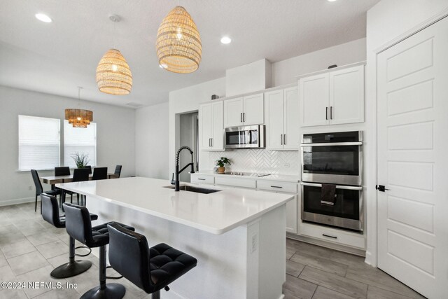 kitchen featuring appliances with stainless steel finishes, sink, pendant lighting, a center island with sink, and white cabinetry