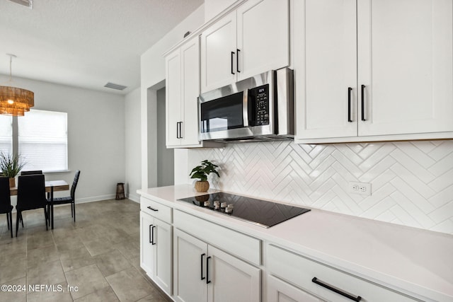 kitchen featuring decorative backsplash, black electric stovetop, a textured ceiling, pendant lighting, and white cabinetry