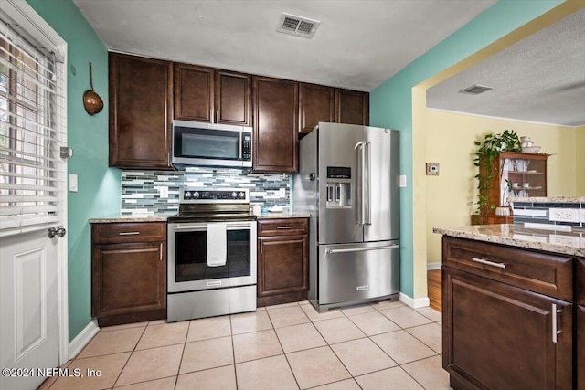 kitchen with dark brown cabinets, light tile patterned flooring, light stone counters, and appliances with stainless steel finishes