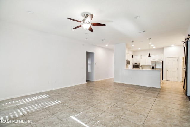 unfurnished living room with ceiling fan, a barn door, light tile patterned floors, and sink