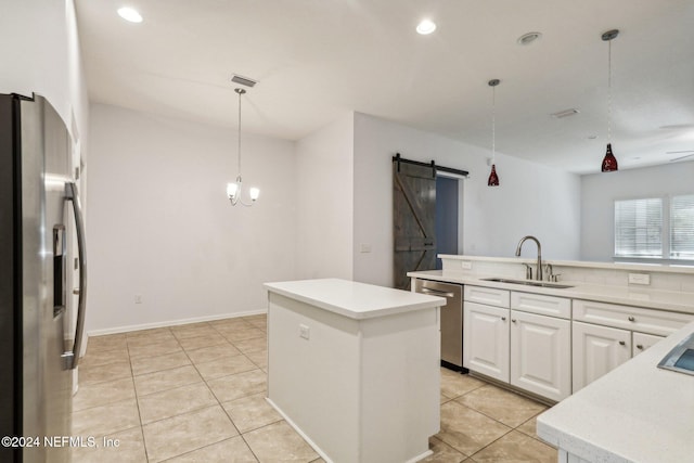 kitchen featuring stainless steel appliances, sink, a barn door, decorative light fixtures, and white cabinetry