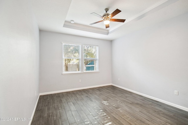 empty room with dark hardwood / wood-style flooring, a tray ceiling, ceiling fan, and ornamental molding