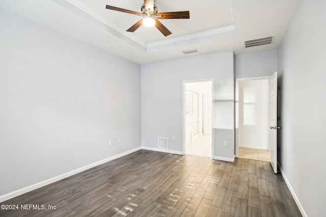 unfurnished bedroom featuring connected bathroom, a tray ceiling, ceiling fan, and dark wood-type flooring