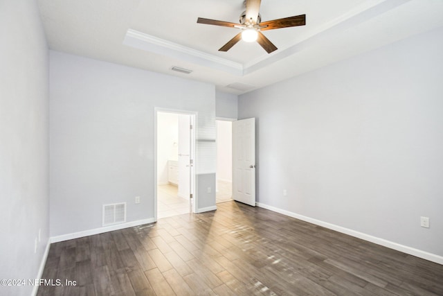 unfurnished bedroom with wood-type flooring, a tray ceiling, ensuite bath, and ceiling fan