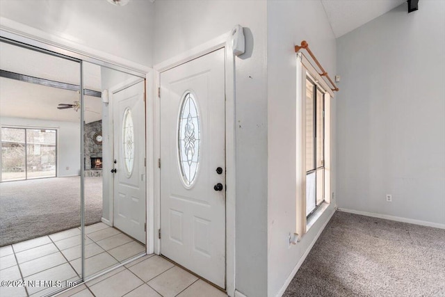 entryway featuring ceiling fan, a stone fireplace, and light colored carpet