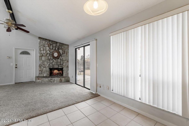 unfurnished living room with lofted ceiling, a stone fireplace, ceiling fan, light tile patterned floors, and a textured ceiling