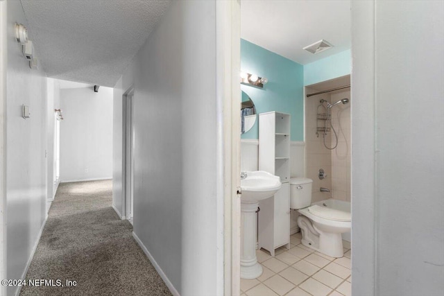 bathroom featuring tile patterned floors, toilet, a textured ceiling, and tiled shower / bath