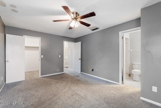 unfurnished bedroom with a walk in closet, ensuite bathroom, a textured ceiling, ceiling fan, and a closet