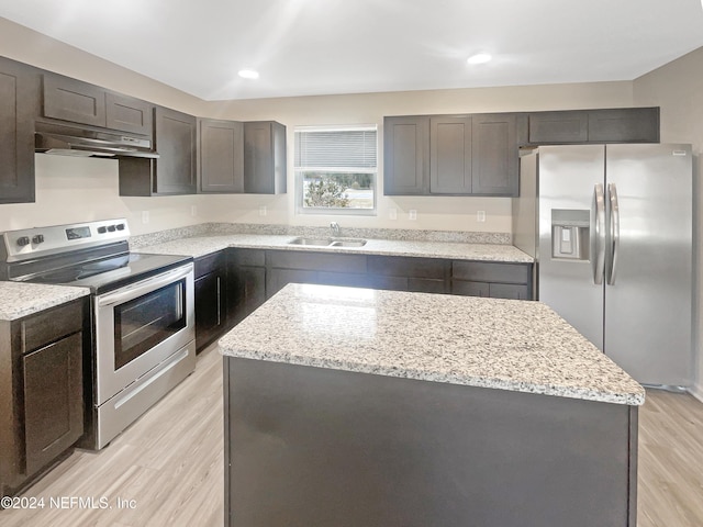 kitchen with light stone countertops, appliances with stainless steel finishes, light wood-type flooring, sink, and a kitchen island