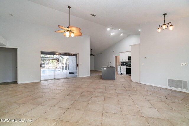 unfurnished living room featuring ceiling fan with notable chandelier, light tile patterned floors, sink, and high vaulted ceiling