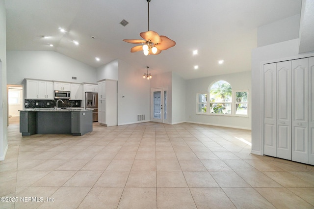 kitchen featuring decorative backsplash, stainless steel appliances, a center island with sink, high vaulted ceiling, and white cabinetry