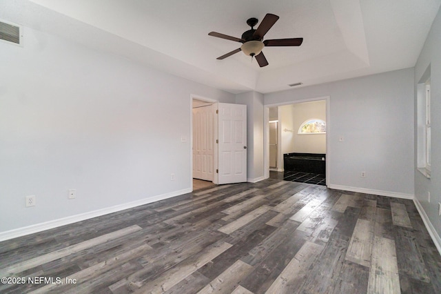 unfurnished bedroom with ceiling fan, dark hardwood / wood-style floors, a raised ceiling, and connected bathroom