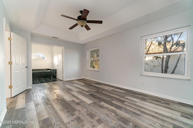 unfurnished bedroom featuring a tray ceiling, ceiling fan, and dark wood-type flooring