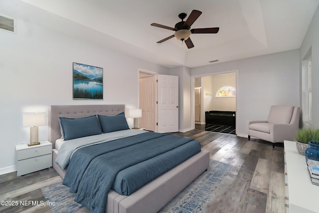 bedroom with ensuite bathroom, ceiling fan, dark hardwood / wood-style flooring, and a tray ceiling