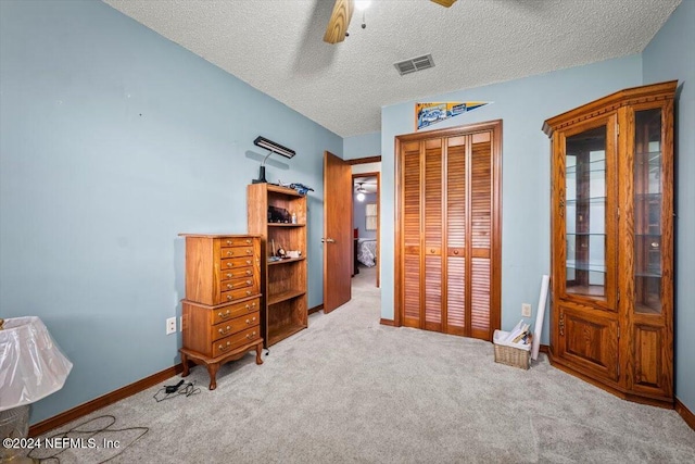 bedroom with ceiling fan, a closet, light carpet, and a textured ceiling