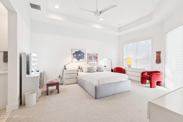 bedroom with light carpet, a raised ceiling, and ceiling fan