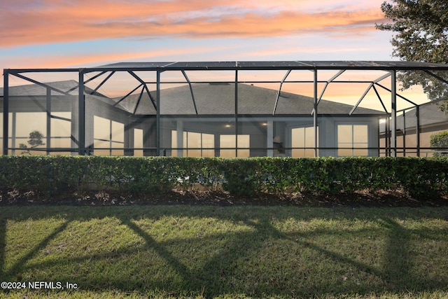 back house at dusk with a lawn and glass enclosure