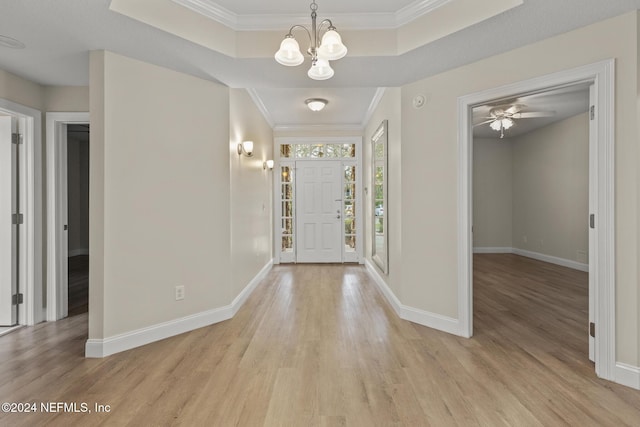 foyer entrance featuring crown molding, a tray ceiling, light wood-type flooring, and baseboards