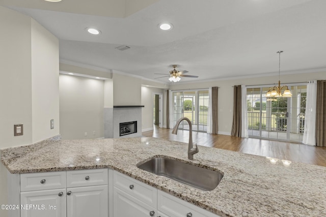 kitchen with a tile fireplace, a sink, white cabinetry, open floor plan, and light stone countertops