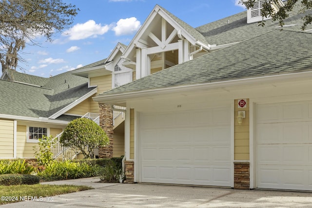 exterior space featuring driveway, a shingled roof, an attached garage, and stone siding