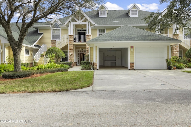 craftsman-style house featuring driveway, stone siding, roof with shingles, an attached garage, and a front yard