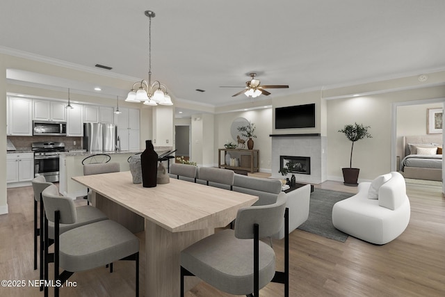 dining room with light wood finished floors, a fireplace, visible vents, and crown molding